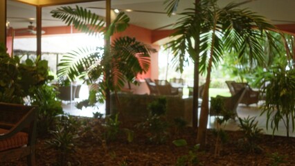 Fototapeta premium Blurred tropical plants in luxury resort lobby with natural light and outdoor view, creating a serene and inviting atmosphere with bokeh effect.