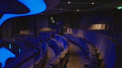 Naklejka premium Curved rows of empty auditorium seats bathed in blue light, softly blurred and defocused interior; background backdrop copyspace backplate.