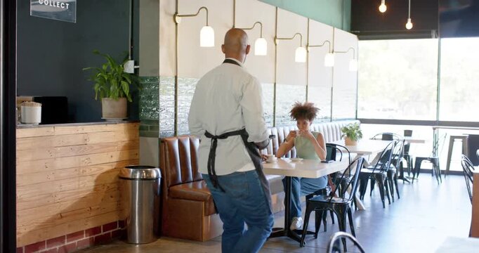 African American women with male server walking from left using tablet taking order at cafe booth