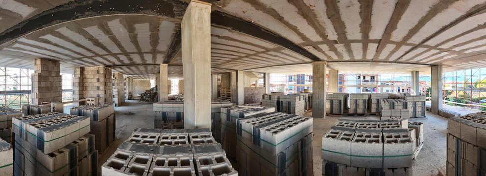 Interior of a construction site with a reinforced concrete structure under construction. Concrete blocks are neatly stacked on the floor, between load-bearing pillars and walls under construction.