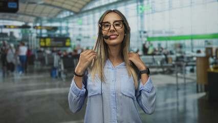Fototapeta premium Woman adjusts headset with hands in airport terminal while smiling and speaking into microphone; friendly customer service.