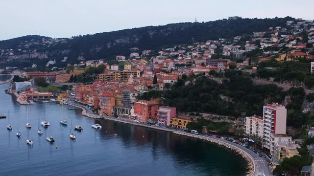 Aerial panoramic 4K video of the picturesque town of Villefranche-sur-Mer, France, featuring the waterfront, beach, railway, historic houses, and luxury yachts in the bay. A stunning drone view of Vil