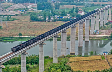 Obraz premium Freight Train on High Viaduct Crossing River Through Rural Landscape