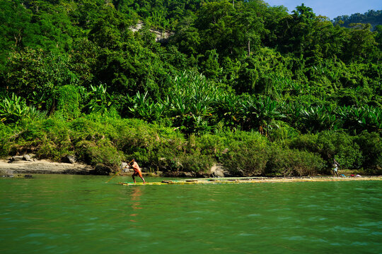 View of a person standing on a raft in a river against a backdrop of lush, vibrant green vegetation, Bandarban, Chittagong Division, Bangladesh.