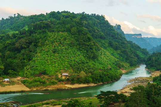 View of a serene river winding through lush green hills, with small buildings nestled along the banks, a tranquil scene of nature's beauty, Bandarban, Chittagong Division, Bangladesh.
