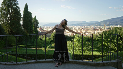 Naklejka premium Woman with bare arms resting on an iron railing, looking out over florence city buildings from a viewpoint overlooking rooftops and hills; serenity.