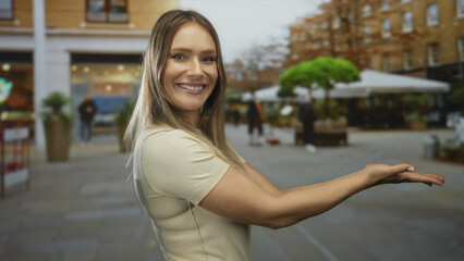 Fototapeta premium Young blonde woman smiling and gesturing outdoors on a city street with people and buildings in the background during daytime