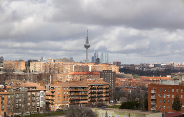 Obraz premium Overcast weather hangs above a dense residential district in Madrid, featuring red brick facades, satellite-covered rooftops, and a tall communication tower.