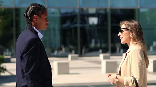 Business partners, a formally dressed man and woman, engage in a lively discussion outside a modern office building, exchanging ideas and smiles