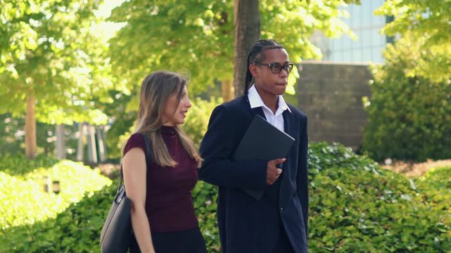 multiethnic Business partners walking and discussing strategy while moving through sunlit financial district, showcasing professional collaboration and diverse teamwork in urban corporate environment