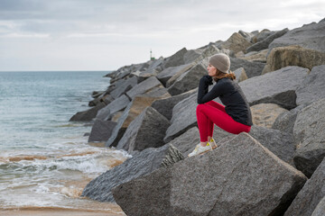 sporty woman sitting on rocks looking out to sea