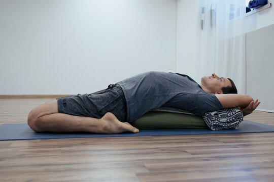 Man lays on yoga bolster at recovery and relaxing Iyengar yoga class