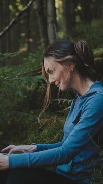 Taking a break from hiking, a young woman sits with her laptop in the carpathian mountains, enjoying the peaceful forest surroundings. Balancing work and adventure, she finds inspiration in nature