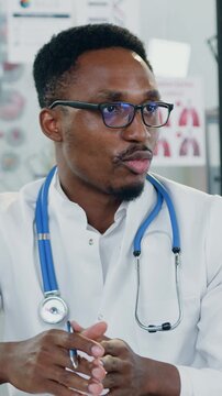 Portrait of good-looking experienced african american man-pediatrician in white gawn with stethoscope which giving consultation to attantive light-haired woman with her 12-aged son during visit to