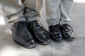 A man and a boy. Father and son. The bond between generations. Both are dressed in classic trousers and classic black leather men's shoes. Care and love in family relationships.