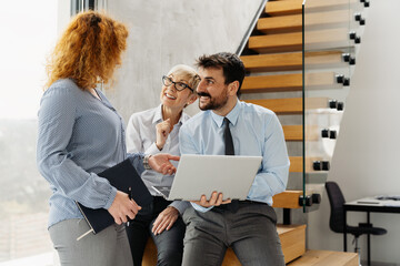 Group of happy coworkers sharing a laugh while a man holds a laptop during a meeting