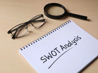 SWOT Analysis hand written on book with wooden table background. business strategy, corporate planning, marketing evaluation concept