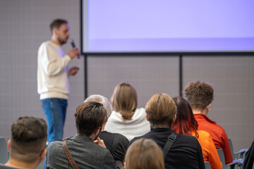 Obraz premium Presenter speaks into microphone while audience listens in modern conference room during workshop.