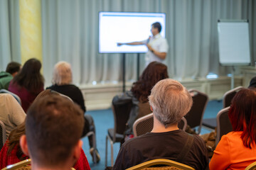 Fototapeta premium Audience attends conference listening to speaker presenting on screen. Attentive crowd in meeting room.