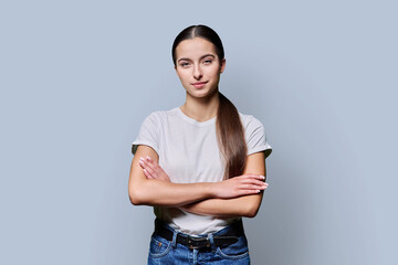 Portrait of beautiful confident teenage girl in white t-shirt on gray background