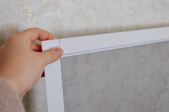 Mosquito screen door with white aluminum frame standing indoors near wall. Concept of home protection, insect prevention, summer season, window and door accessories.