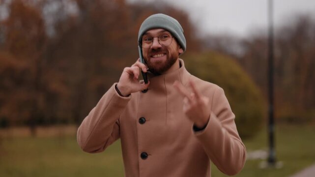 Happy Young Man Talking on Mobile Phone in an Autumn Park