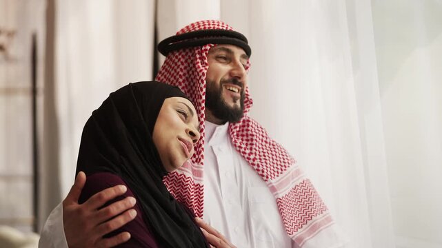 Loving Arab husband and wife embracing near window, care and emotional support
