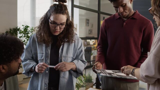 Low angle tilt-up shot of group of diverse colleagues discussing work, gathred at table in design bureau office