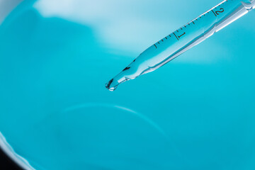 Macro Shot of Water Droplet Falling from Glass Pipette on Blue Background,A close-up, high-speed macro photograph capturing a single, crystal-clear liquid drop falling from the tip of a glass dropper.
