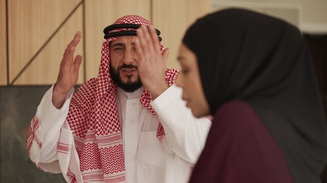 Muslim man in traditional ghutrah arguing with displeased wife at home
