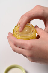 Woman applying cosmetic cream to skin. Hands holding open jar of face cream, cosmetic product with one hand. Skincare, moisturizer, beauty treatment, care, cosmetic texture, close-up.