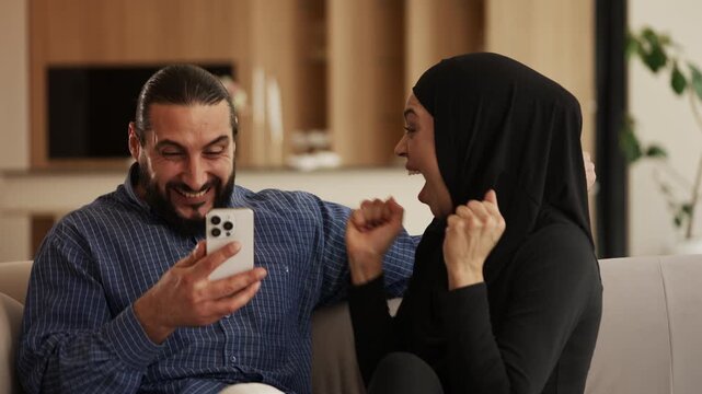 Modern Muslim couple celebrating funding win after reading message on phone