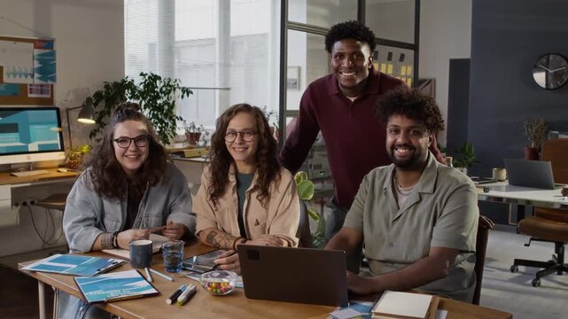 Portrait shot of team of smiling diverce designers working on project at desk in modern design bureau office