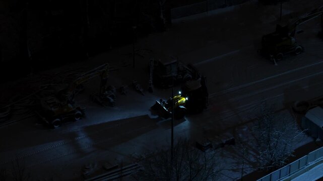 Tractor driving on a snowy road at night on a construction site highlighting winter work, heavy machinery operation and industrial activity in cold weather conditions