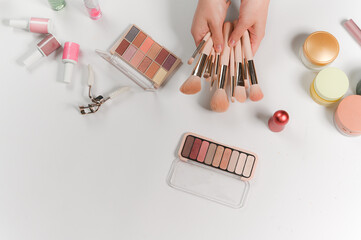 Makeup products arranged on a white background. Brushes in hands, eyeshadow palettes, nail polishes, and cosmetic accessories. 