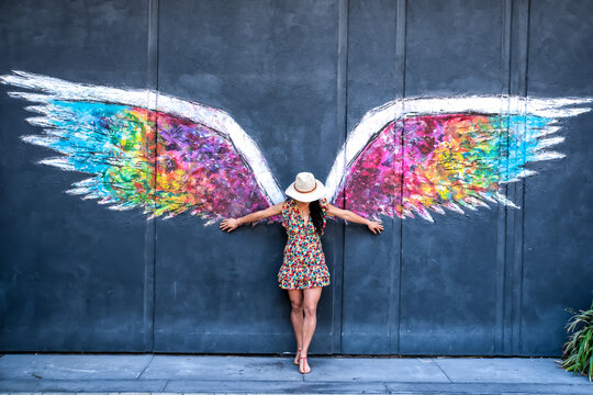 A woman stands in front of a mural of a winged angel