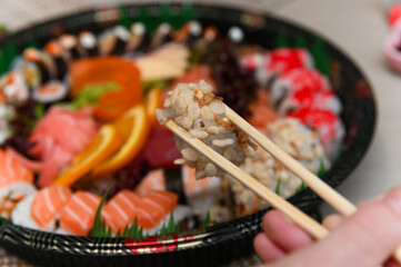 A woman holding chopsticks. A takeout sushi box. A maki sushi roll filled with a variety of fresh ingredients. A vibrant assortment of fresh sushi, including nigiri, rolls, and sashimi, beautifully ar