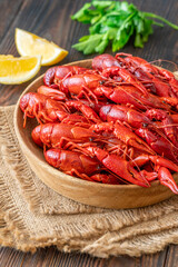 Wooden bowl of bright red boiled crawfish with lemon and parsley, rustic table