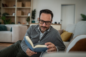 Man reading book relaxing in modern home living room