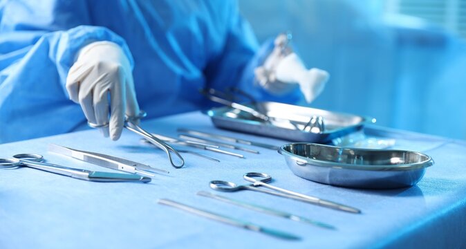 Doctor with different surgical tools at table in hospital, closeup
