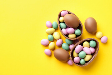 Obraz premium Happy Easter. Tasty chocolate eggs with colorful candies on yellow background, flat lay. Space for text