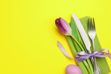 Easter celebration. Festive table setting with floral decor and painted egg on yellow background,...