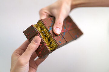 Hands breaking a thick Dubai chocolate bar to reveal the crunchy green pistachio cream and kunafa pastry filling.