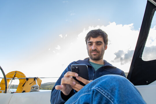 Man relaxing on a sailboat using smartphone in Lofoten