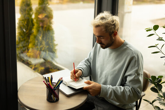 A man takes notes in a book while sitting at a table in a cozy cafe