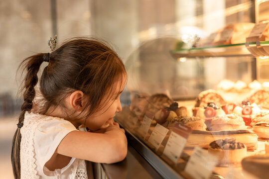 Young girl gazing at tempting pastries in bakery display