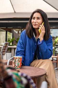 Woman on phone holding coffee in modern cafe