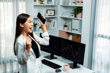 Successful young Asian businesswoman earning high profit raising fist up, holding smartphone in...