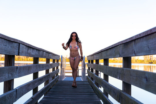 A woman in a bikini is walking across a wooden bridge over a body of water