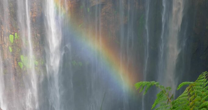 Close-Up Detail of Tumpak Sewu Waterfall with Rainbow Over Mossy Cliff, Indonesia
